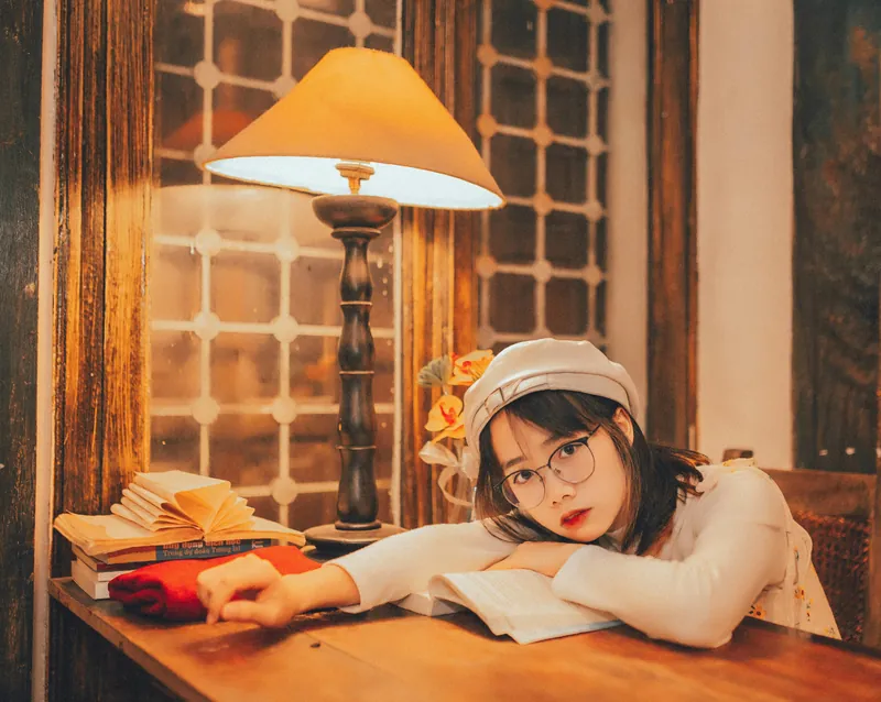 Picture of a stylish young woman leaning over a desk with a warm lamplight glowing above her