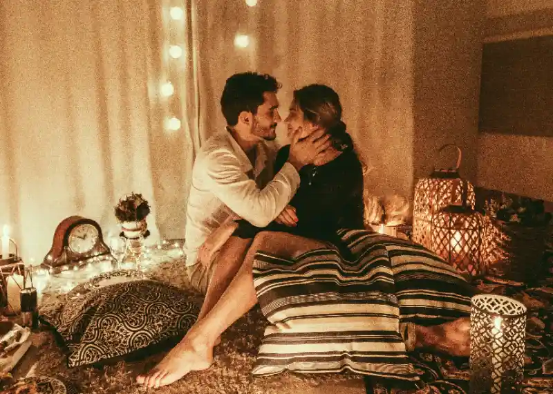 A couple kiss each other on blankets surrounded by candles