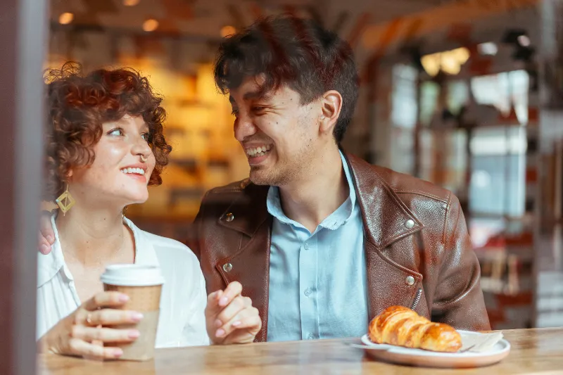 A man and a woman stand at a coffee bar smiling at each other