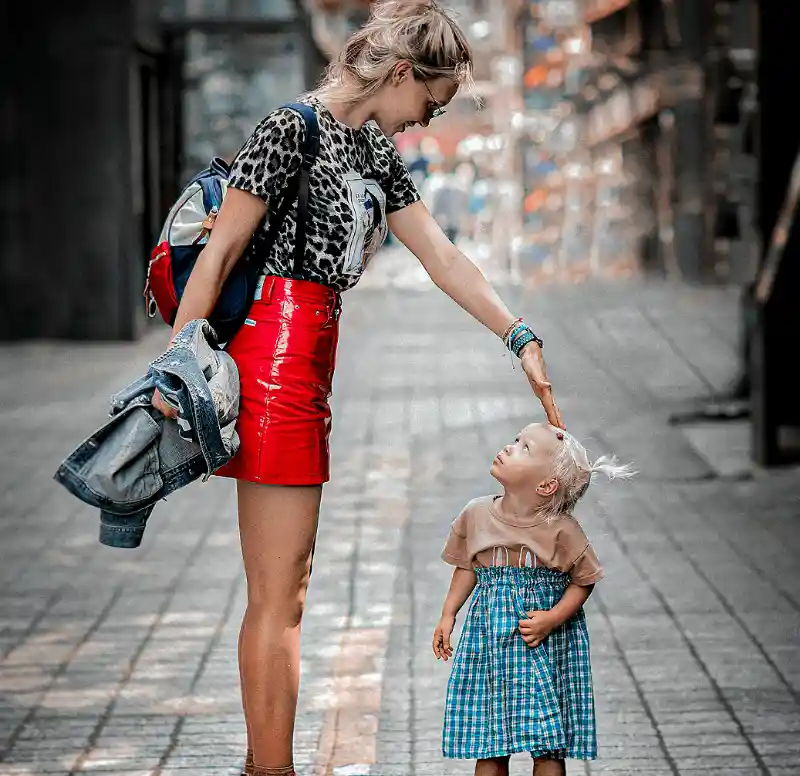 An adult woman stands on her tiptoes and taps a small girl on the head