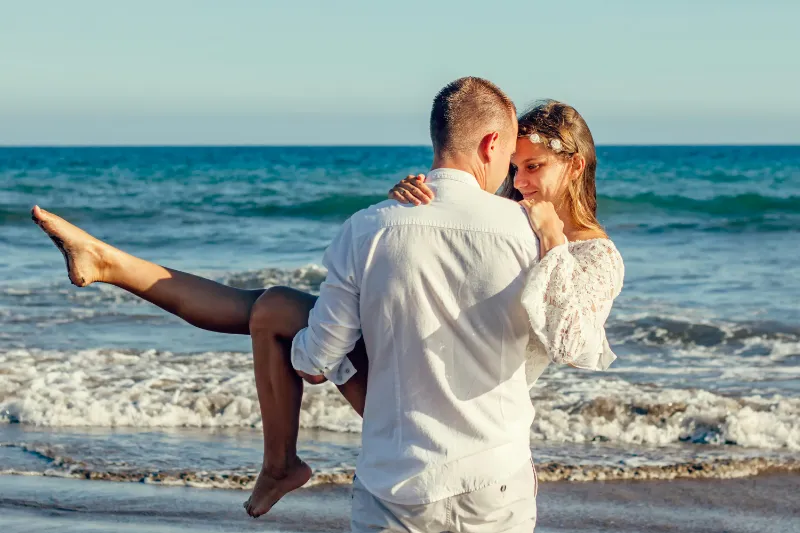 A man princess-carrying a woman on the beach