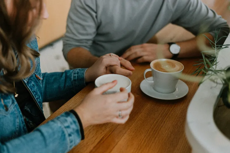 Two people sitting and talking at a cafe, holding hands.