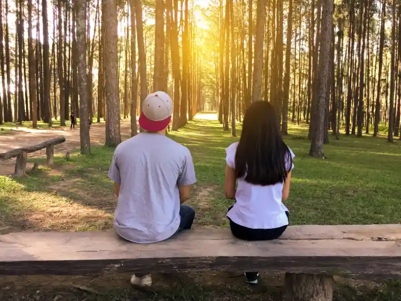 A couple sits on a bench, looking into the trees in the distance