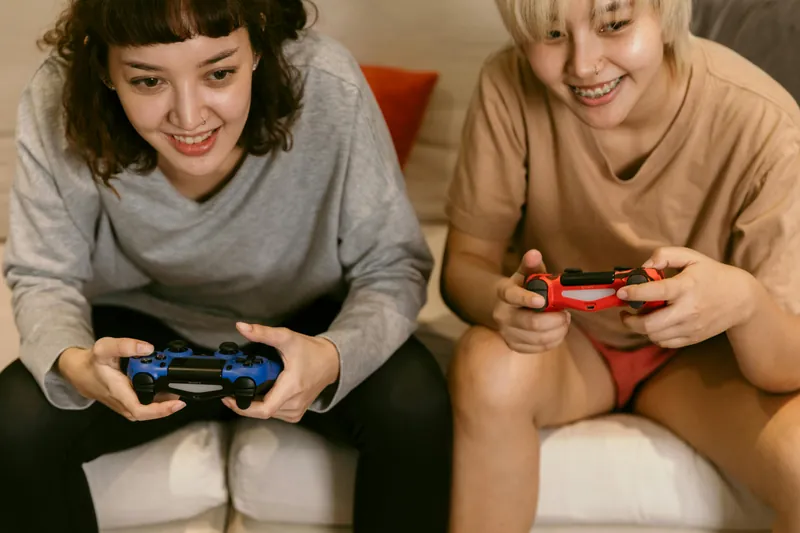 A couple sitting on a couch playing video games together. Both are smiling and looking intently at the screen.