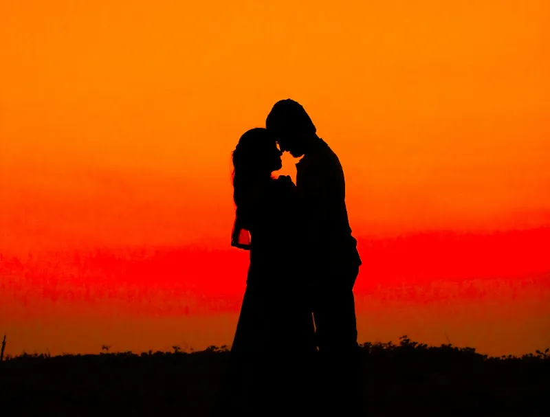 Two people embrace each other with a soft sunset behind them